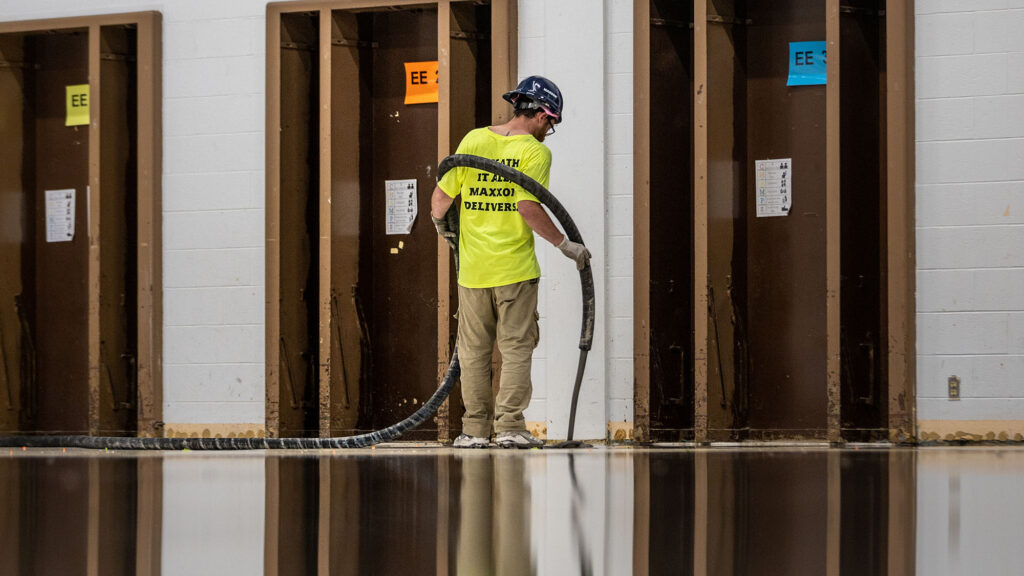 A Maxxon applicator wearing a yellow shirt, khakis and a hard hat is installing self-leveling underlayment. 