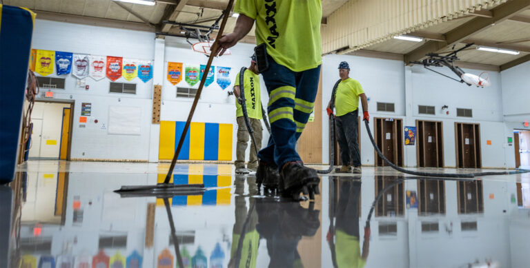 Three Maxxon applicators wearing neon safety shirts, boots and dark pants are installing self-leveling underlayment.