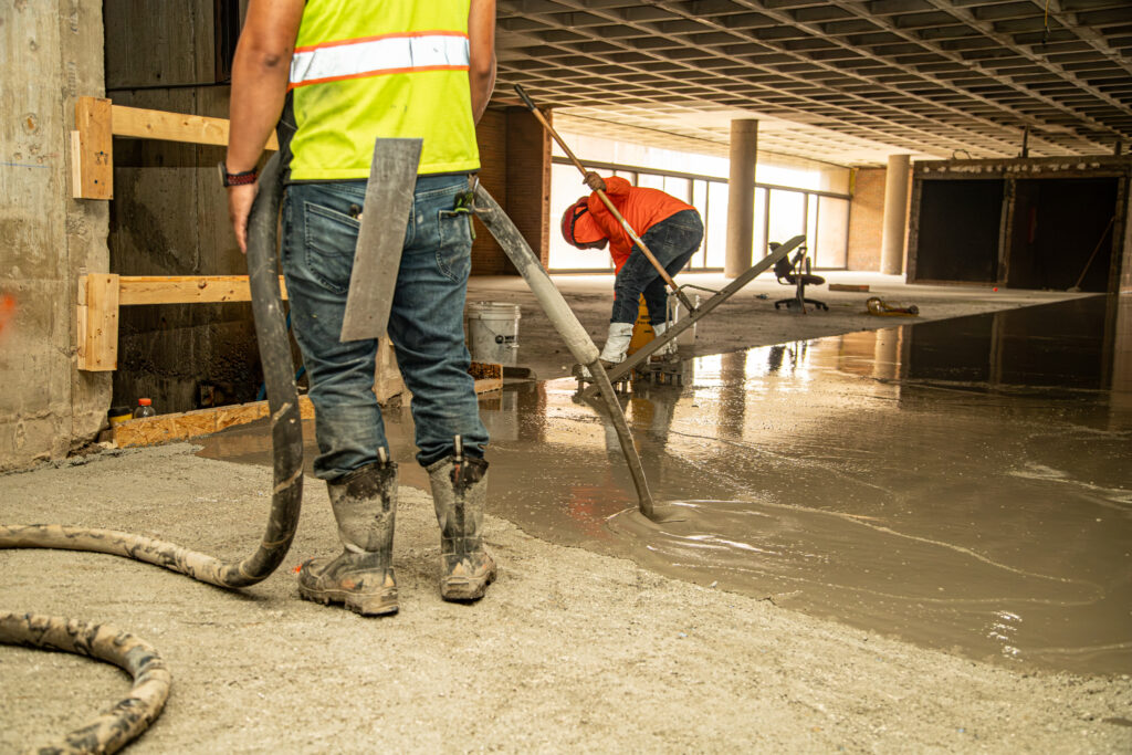 Worker pouring Maxxon Level EZ across the concrete slab at the University of Tennessee Presidential Court Building.